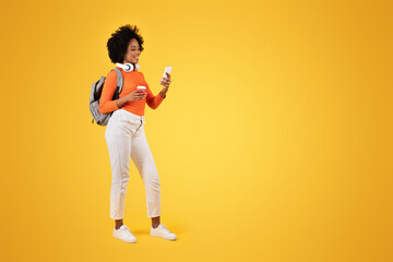 Engaged young woman with a curly afro casually strolling, looking at her smartphone and smiling