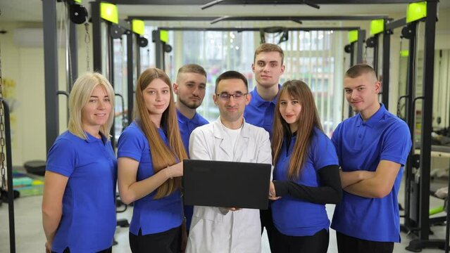 A group of people in blue shirts are posing for a picture with a man in a lab coat holding a laptop