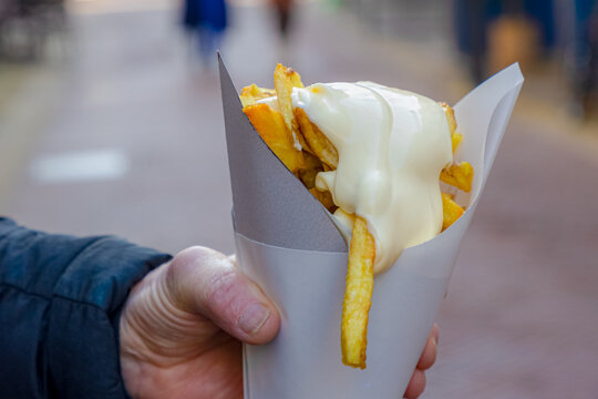 Selective focus of a man hand holding french fries, Friet or Patat with mayonnaise on top, Fritessaus or frietsaus is a Dutch accompaniment to French fries, Served popularly nationwide, Netherlands.