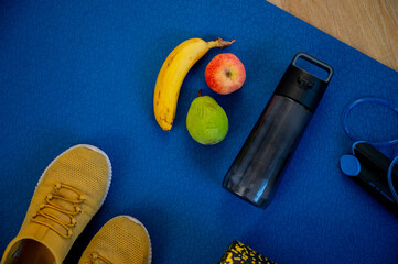 A medley of tropical fruits and a resistance band on the workout mat. Energizing the body for strength training - 747593474