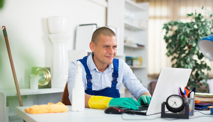 Office cleaner in overalls plays on laptop instead of cleaning the office