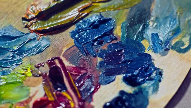 Different paints on the wooden palette. Oil paint on the artist’s palette. Camera panoramic move over the artist’s palette.  