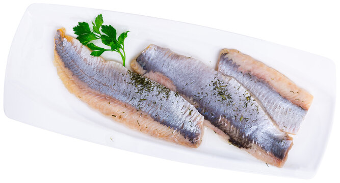 There is of salted herring appetite sild fillet seasoned on white ceramic plate decorated with parsley. Traditional Russian snack. Isolated over white background