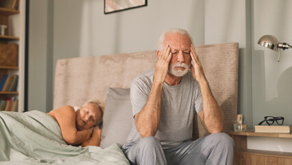 Worried senior man sitting on bed in his bedroom