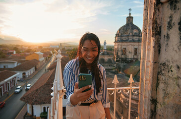 A smiling young latin woman dressed in casual wear and using a smartphone