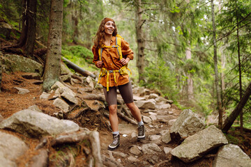 Beautiful traveling woman  in the mountains on a background of a forest. Hiking, active lifestyle. Outdoor recreation concept.