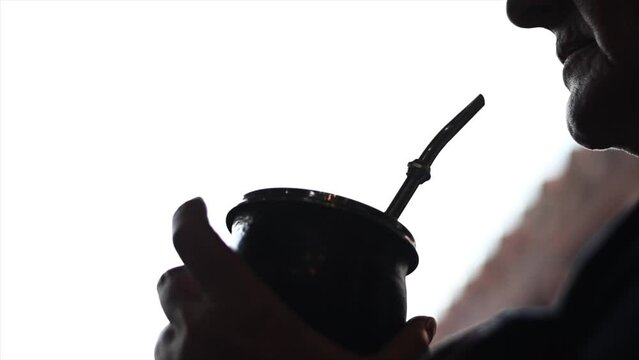 video in slow motion behind light of an unrecognizable person drinking mate traditional Argentine drink of yerba and water in tumba and porongo