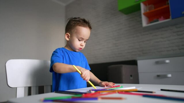 Two year old baby boy chooses and draws with a long yellow pencil. Little kid doing art activity at home. Low angle view.
