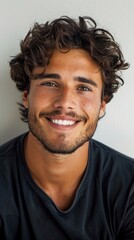 Obraz premium A young man with curly hair wearing a black shirt smiles at the camera in a close-up portrait.