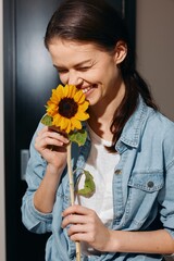 Joyful young woman holding a sunflower, radiating happiness and beauty in a sunny field of blooming floral bliss.