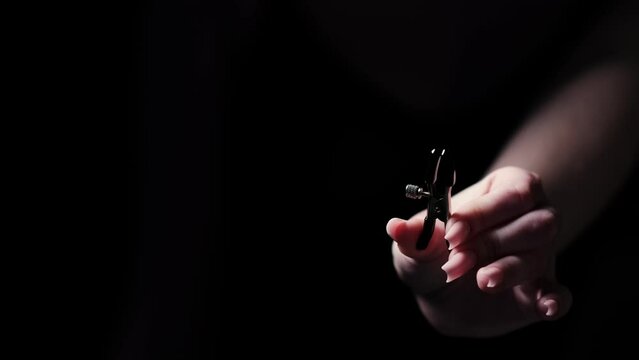 Metal BDSM nipple clamp in a woman's hand on a black background. Sex products, sex toys, adult gifts for couples.
