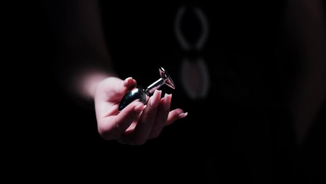 Metal anal plug with a blue crystal in the hand of a girl on a black background. Sex shop, Adult store. BDSM - outfit for adult sex games
