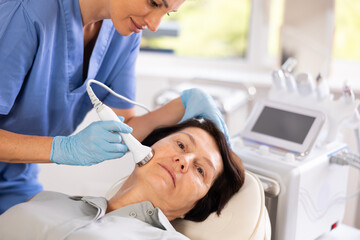 Aged female patient receiving facial procedure with high frequency ultrasonic vibration attachment...