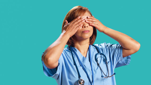 Certified nursing professionist covering eyes, ears and mouth with hands, imitating the three wise monkeys. Nurse showing don`t see, don`t hear and don`t speak concept, isolated over studio background