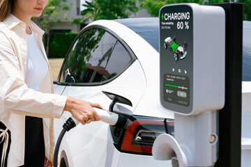 Young woman put EV charger to recharge electric car's battery from charging station. Alternative...