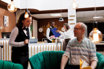 Senior woman checks in at hotel front desk, eager for pleasant holiday. Eldery female client fills...