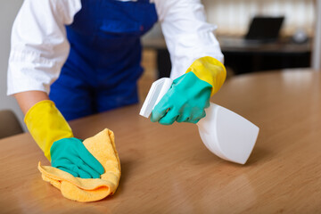 Worker in rubber gloves cleaning table with rag and detergent in hand-pumped sprayer.