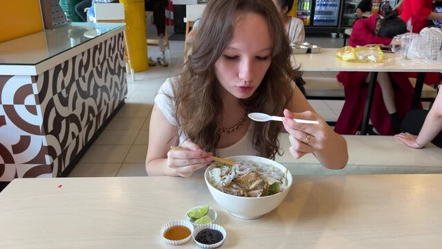 A young girl eats delicious pho bo soup with chicken in Vietnam in the mall fast cooking cheap food healthy traditional Vietnamese soup in Ho Chi Minh City. Saigon