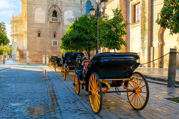 Fototapeta na wymiar A row of empty horse drawn carriages with their traditional yellow wheels line up waiting for tourists in the morning by the cathedral, in the Andalusian city of Seville, Spain.