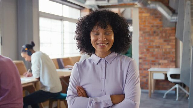Portrait of smiling businesswoman working in modern open plan office turning to  look at camera with colleagues in background - shot in slow motion