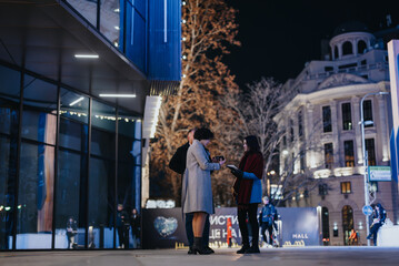 Two friends meeting for night out in urban cityscape with warm lighting.