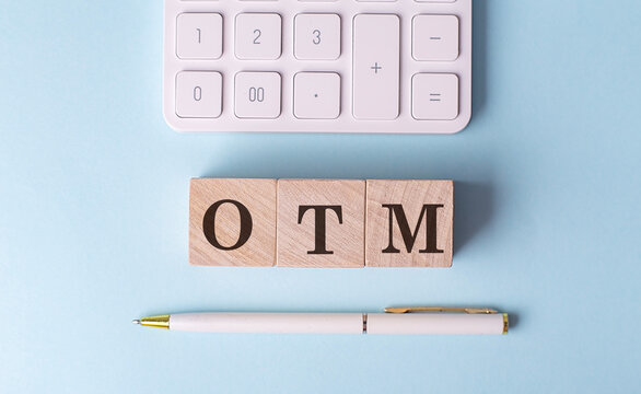 OTM -OUT OF MONEY on wooden cubes with pen and calculator, financial concept