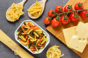 Raw fusilli in bowl and spaghetti, penne, tagliatelle on grey background.