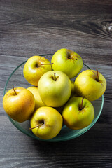 Top view of a set of juicy apples in a glass bowl on wooden background.