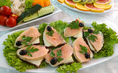 sandwiches with red fish for a snack on the buffet table. decorated with olives, lettuce leaves and sprigs of herbs. delicious snack or appetizer