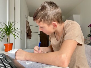  A teenage boy does homework in front of a computer monitor.