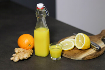Homemade orange, lemon and ginger drink in a glass bottle with a small shot glass