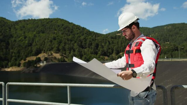 Engineer with white helmet holds a project of the new dam