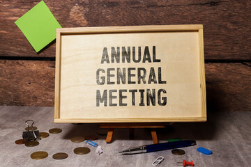 On a light background, a white notebook with are words AGM Annual General Meeting and a pen.