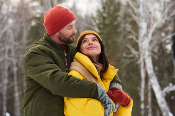 Young Caucasian man and woman in love hiking on frosty winter day hugging and flirting, copy space
