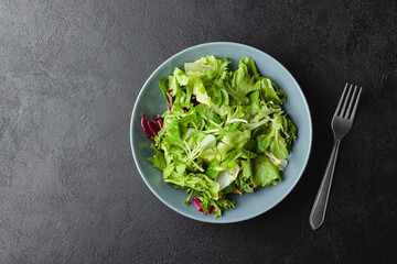 Green salad leaves in bowl on black table.