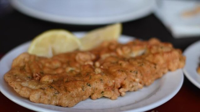 slow motion video of plate of fried hake filet with lemon