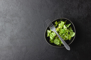 Green salad leaves in bowl on black table.