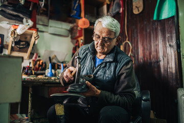 A senior cobbler is fixing shoes at his small workshop.