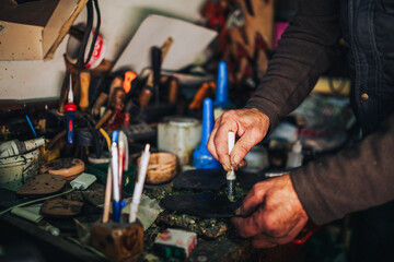 Close up of old cobbler's hands putting glue on outer sole at shop.