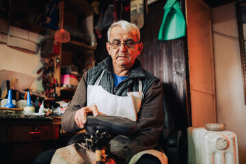 A senior cobbler is fixing an old boot in his workshop.