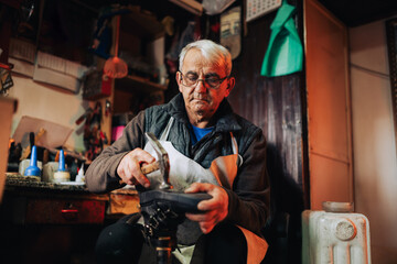 A senior artisan is repairing an old boot in his workshop.