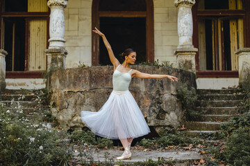 Prima ballerina dancing gracefully in front of old rustic building.