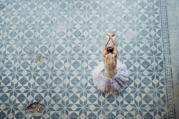 Top view of ballerina in figure against blue rustic tiled floor.