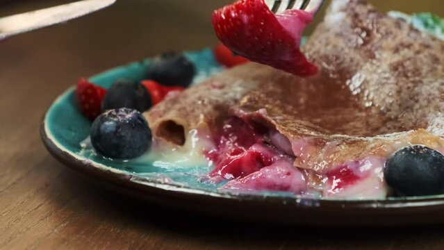Young woman impales strawberry on fork from plate with pancake closeup. Young woman artfully commences consumption of chef-prepared dessert