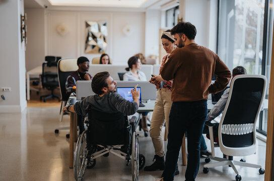 A modern office scene captures a dynamic team including a professional in a wheelchair discussing ideas and collaborating in a bright workspace.