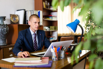 Portrait of successful businessman confidently working on laptop in modern business office