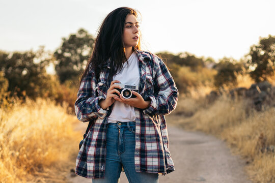 Young woman taking photos with analog camera in the field at sunset