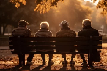 Poster  Four elderly people sit on a park bench, silhouetted against an autumn background, a scene of friendship and contemplation. © Margo_Alexa