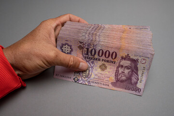 A man is holding a Hungarian paper forint in his hand. Against a gray background. Concept showing...