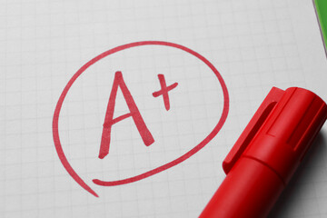 School grade. Red letter A with plus symbol on notebook paper and marker, closeup
